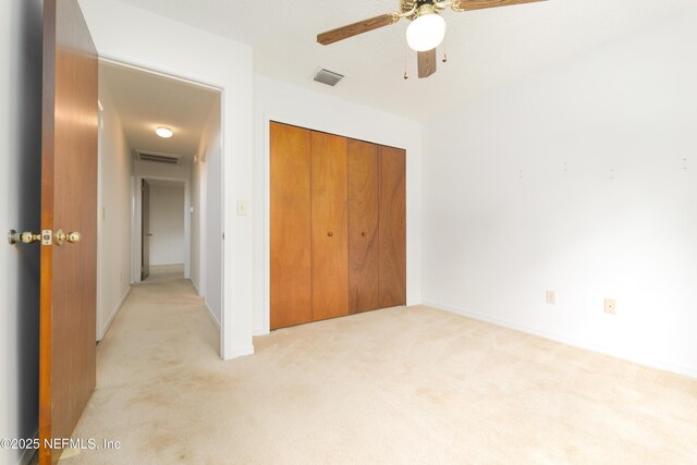 unfurnished bedroom featuring ceiling fan, visible vents, a closet, and light carpet