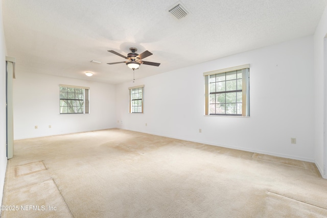 unfurnished room with visible vents, light colored carpet, a textured ceiling, and a healthy amount of sunlight