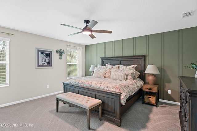 carpeted bedroom with a decorative wall, baseboards, visible vents, and ceiling fan