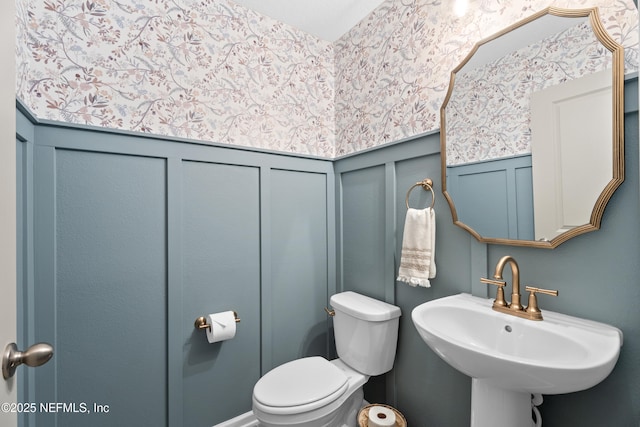 bathroom with a wainscoted wall, toilet, a decorative wall, and a sink