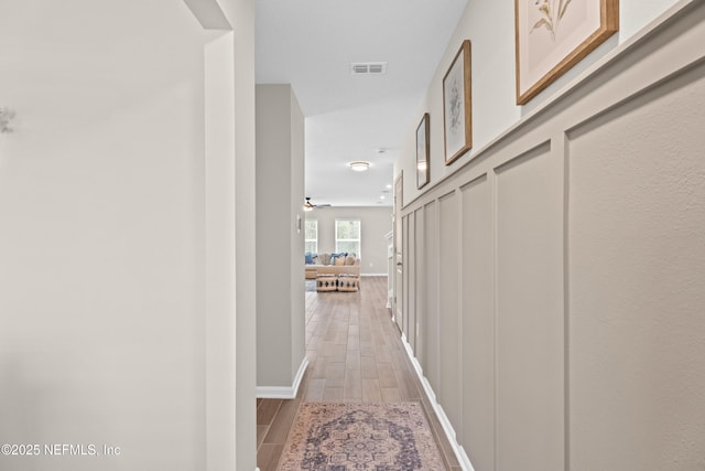 hall with wood finish floors, visible vents, and baseboards