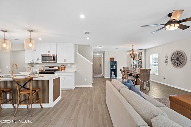 living area featuring visible vents, baseboards, light wood-type flooring, recessed lighting, and ceiling fan with notable chandelier