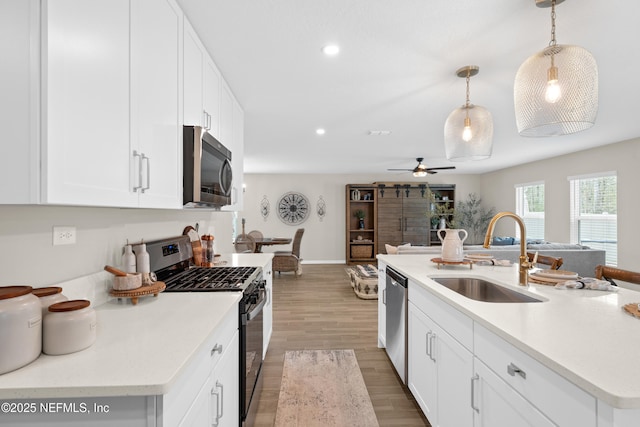 kitchen with pendant lighting, a sink, open floor plan, stainless steel appliances, and light wood-style floors