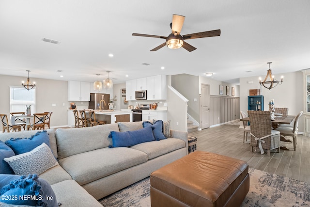 living area featuring stairway, visible vents, recessed lighting, ceiling fan with notable chandelier, and light wood-type flooring