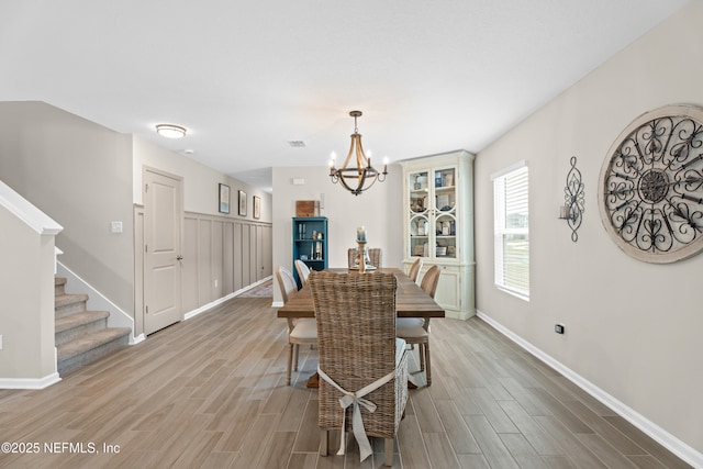 dining area with stairs, a notable chandelier, light wood-style floors, and baseboards