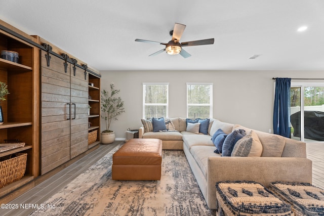 living room with a barn door, a healthy amount of sunlight, wood finished floors, and a ceiling fan