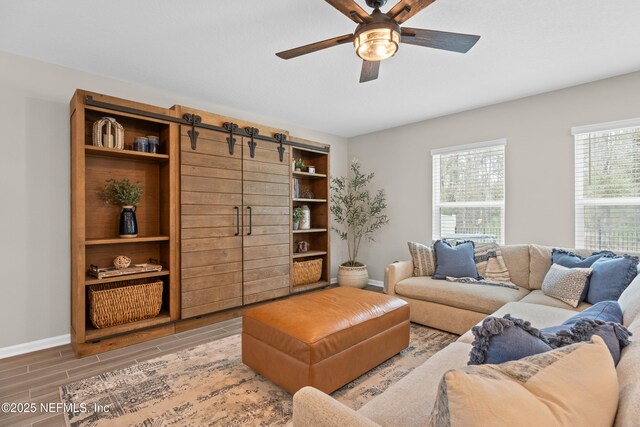 living room with a barn door, baseboards, a ceiling fan, and wood tiled floor