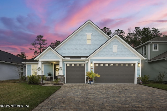 view of front of house featuring a garage, stone siding, a front lawn, and decorative driveway