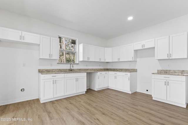 kitchen featuring light stone counters, baseboards, light wood finished floors, a sink, and white cabinets