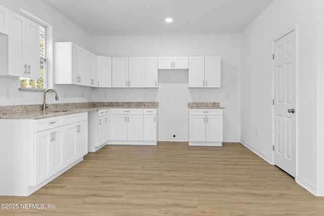 kitchen featuring a sink, light stone counters, light wood-style floors, and white cabinetry