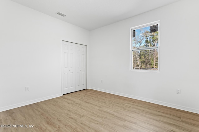 unfurnished bedroom featuring visible vents, baseboards, a closet, and light wood-style flooring