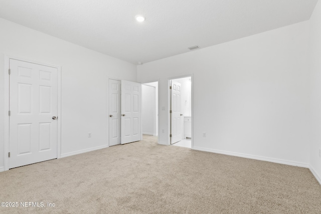 unfurnished bedroom featuring visible vents, baseboards, ensuite bathroom, and carpet flooring