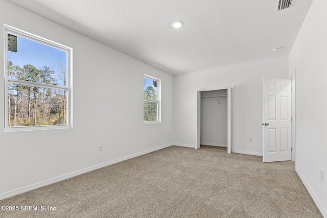 unfurnished bedroom with visible vents, a textured ceiling, a closet, carpet floors, and baseboards