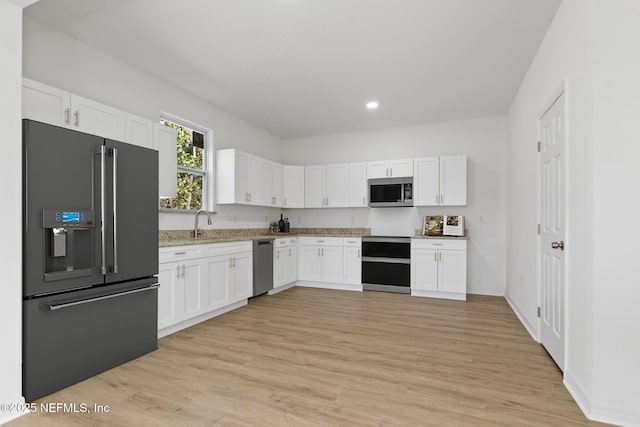 kitchen featuring light stone counters, light wood-style flooring, white cabinets, stainless steel appliances, and a sink