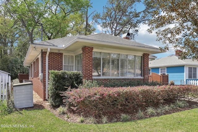 view of front of property featuring a sunroom, brick siding, a chimney, and a shingled roof