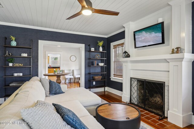living room featuring wood finished floors, a ceiling fan, ornamental molding, wooden ceiling, and a brick fireplace