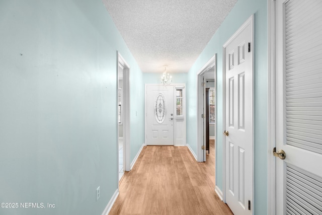 hallway with a notable chandelier, a textured ceiling, light wood-type flooring, and baseboards