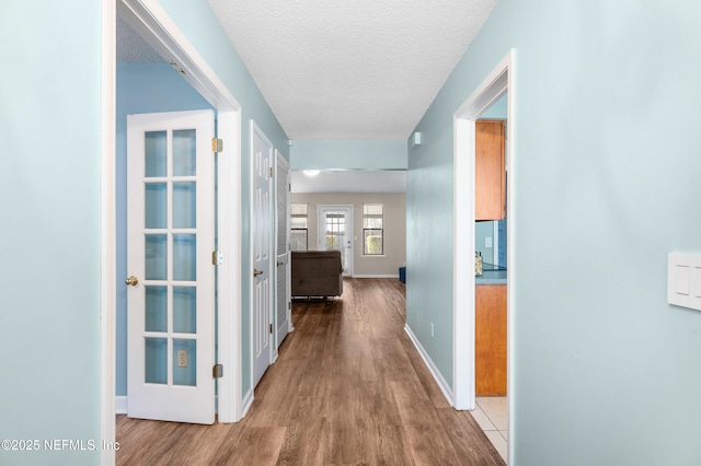 corridor with baseboards, a textured ceiling, and wood finished floors