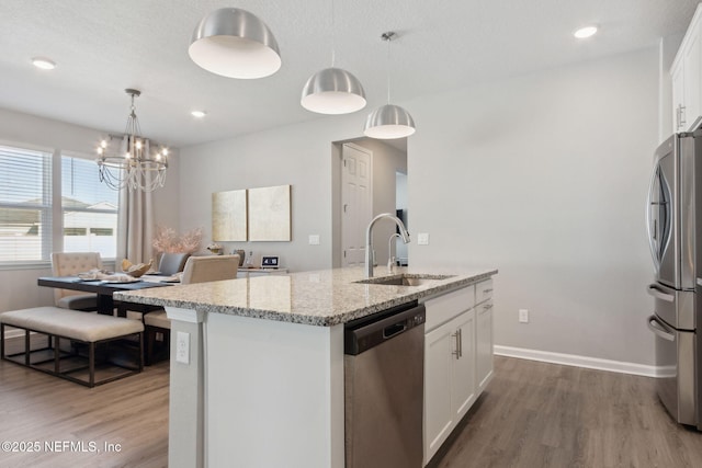 kitchen featuring wood finished floors, appliances with stainless steel finishes, a sink, and a kitchen island with sink