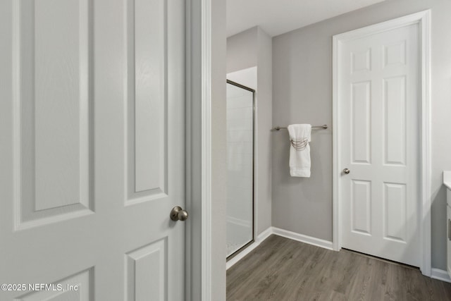 full bath featuring a shower stall, baseboards, and wood finished floors