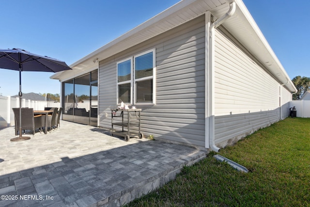 view of side of home featuring a patio, a lawn, fence, and a sunroom