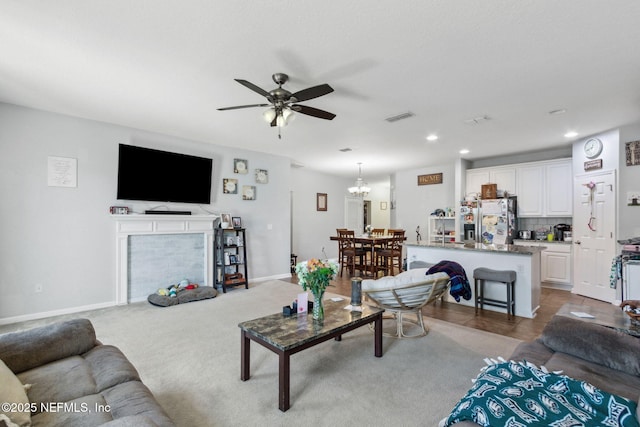 carpeted living area featuring visible vents, baseboards, a fireplace, recessed lighting, and ceiling fan with notable chandelier