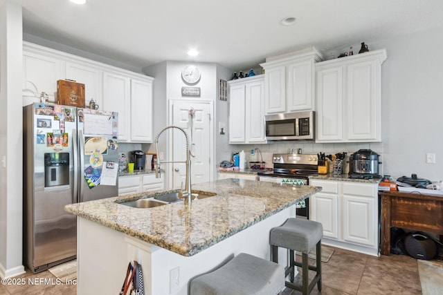 kitchen featuring an island with sink, a sink, decorative backsplash, white cabinets, and appliances with stainless steel finishes