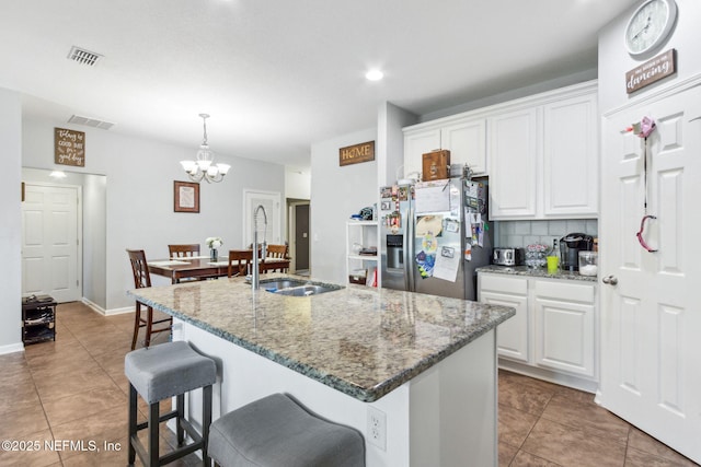 kitchen with visible vents, decorative backsplash, white cabinets, stainless steel fridge, and a sink