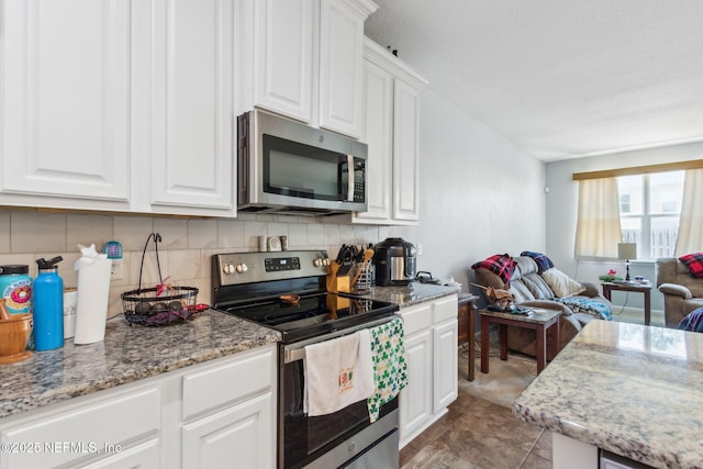 kitchen with backsplash, open floor plan, light stone counters, appliances with stainless steel finishes, and white cabinets