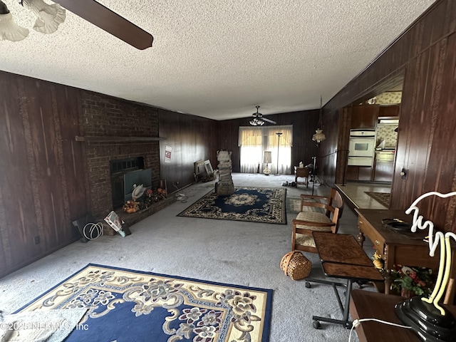 unfurnished living room featuring wooden walls, ceiling fan, carpet flooring, a fireplace, and a textured ceiling