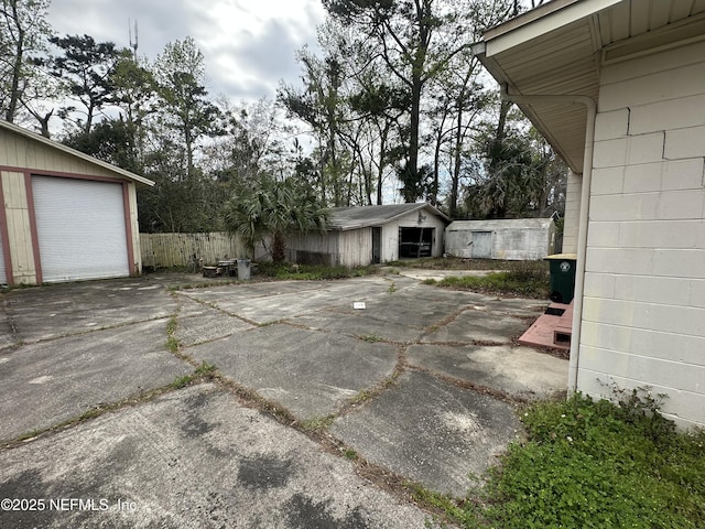 exterior space featuring a garage, concrete driveway, an outdoor structure, and fence