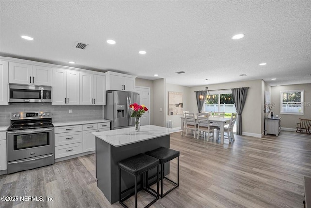 kitchen with a wealth of natural light, backsplash, light wood-type flooring, and appliances with stainless steel finishes