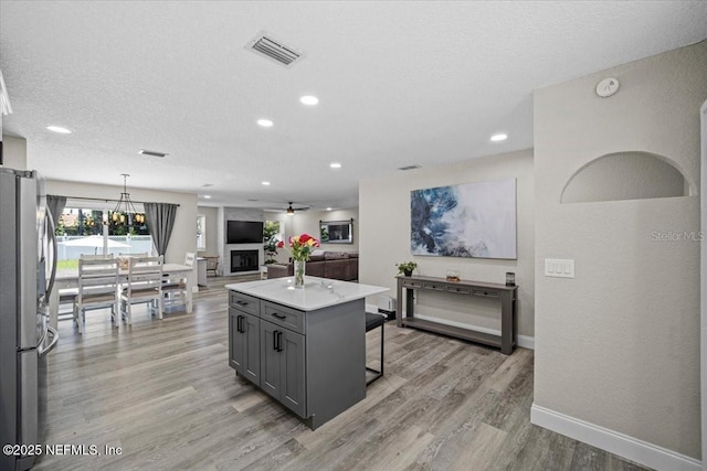 kitchen with visible vents, a kitchen bar, gray cabinetry, light wood-style flooring, and freestanding refrigerator