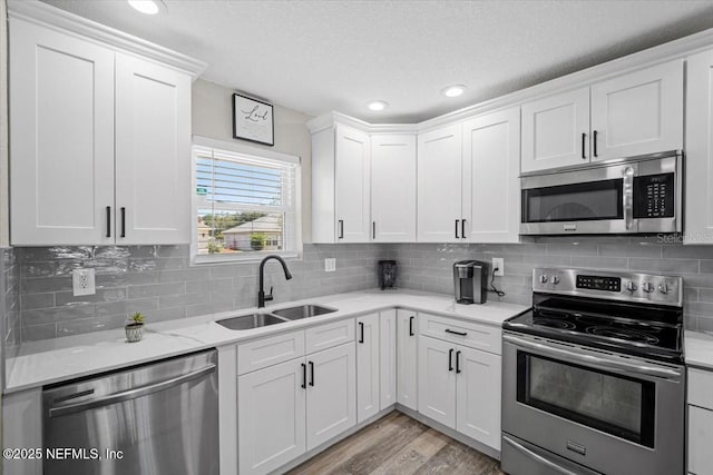 kitchen with light wood finished floors, tasteful backsplash, appliances with stainless steel finishes, white cabinetry, and a sink