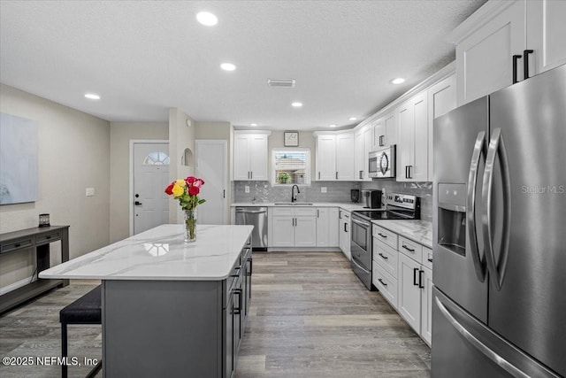 kitchen with a sink, a kitchen island, backsplash, appliances with stainless steel finishes, and light wood finished floors