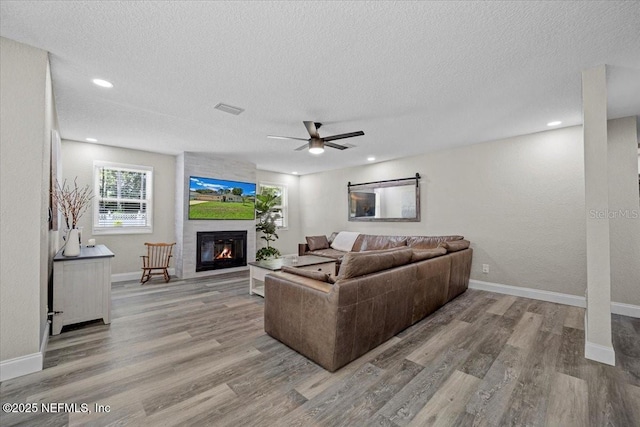 living area featuring visible vents, a textured ceiling, wood finished floors, a large fireplace, and baseboards