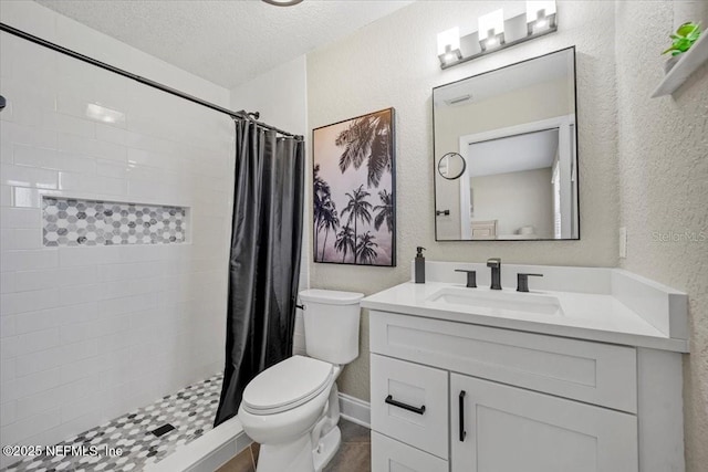 bathroom with toilet, a textured ceiling, a tile shower, vanity, and a textured wall