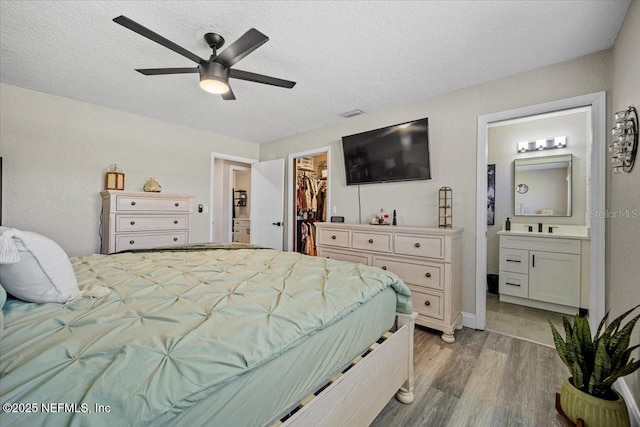 bedroom featuring light wood-type flooring, a walk in closet, ensuite bathroom, a textured ceiling, and a closet