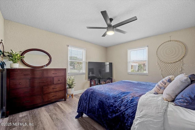 bedroom with a ceiling fan, multiple windows, wood finished floors, and a textured ceiling