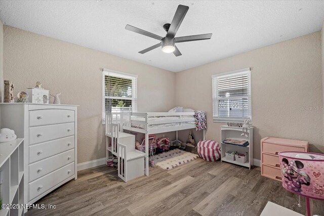 bedroom with baseboards, wood finished floors, a ceiling fan, and a textured wall