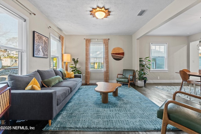 living area featuring a wealth of natural light, visible vents, a textured ceiling, and wood finished floors