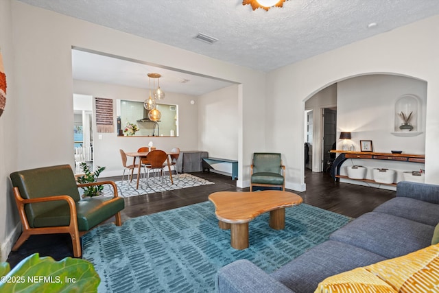 living room with visible vents, baseboards, wood finished floors, arched walkways, and a textured ceiling