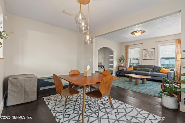 dining area featuring wood finished floors, arched walkways, and a textured ceiling