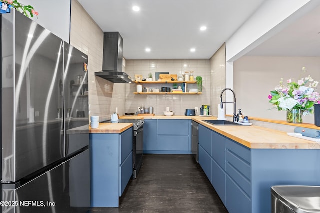 kitchen with electric range, butcher block countertops, a sink, freestanding refrigerator, and wall chimney range hood