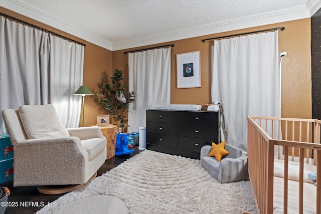 bedroom with a textured wall, crown molding, a nursery area, and wood finished floors