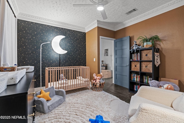 bedroom featuring visible vents, ornamental molding, a textured ceiling, wood finished floors, and ceiling fan