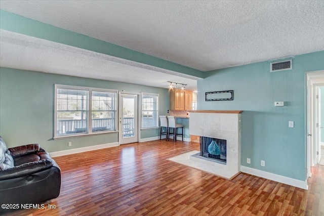 unfurnished living room featuring wood finished floors, visible vents, baseboards, a textured ceiling, and a tiled fireplace