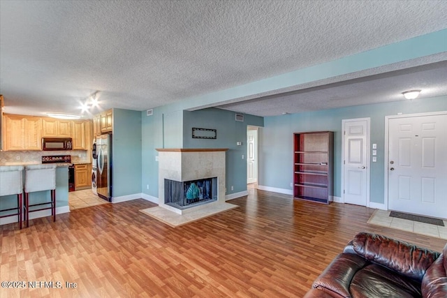 living room featuring a tiled fireplace, light wood-style floors, and baseboards