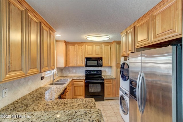 kitchen with light tile patterned floors, light stone counters, a sink, black appliances, and stacked washer / dryer