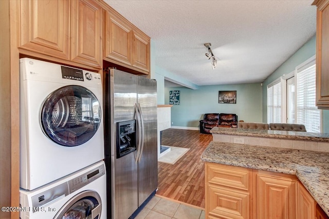 laundry room featuring light tile patterned floors, laundry area, stacked washer and clothes dryer, rail lighting, and a textured ceiling